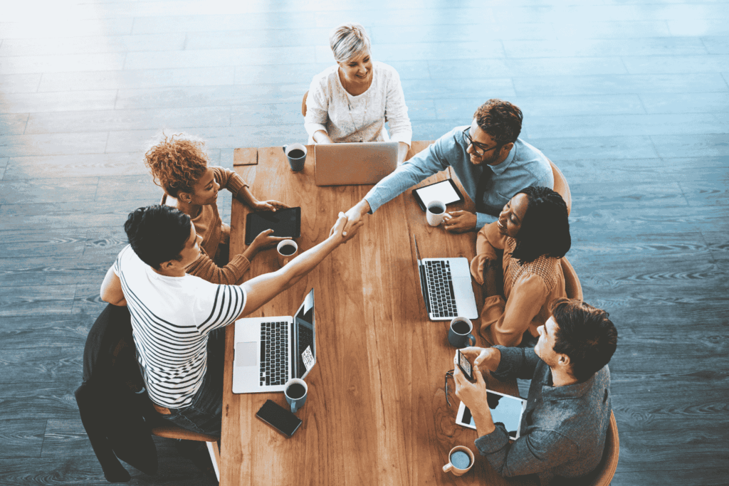 Employees gathered around a table as one welcomes a new hire with a handshake, representing a successful onboarding automation outcome.