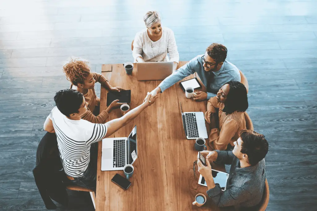 Employees gathered around a table as one welcomes a new hire with a handshake, representing a successful onboarding automation outcome.