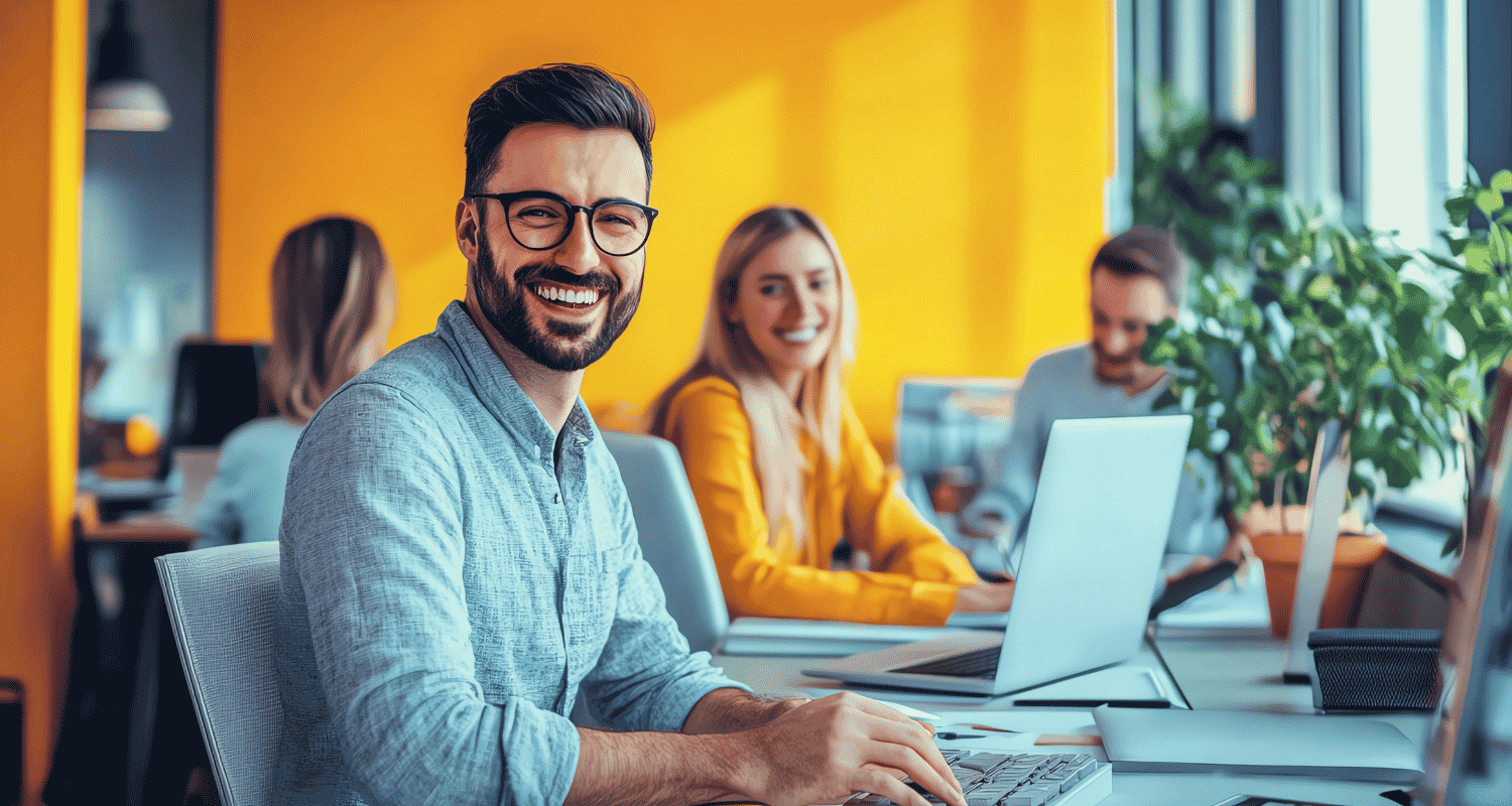 Happy employee using a laptop to collaborate with coworkers, demonstrating how managed IT improves employee productivity through reliable technology and secure access.